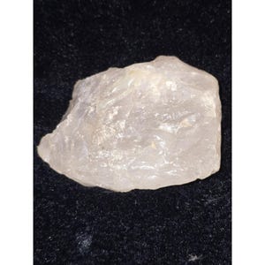 May include: A translucent, rough-cut quartz crystal with a slightly cloudy appearance. The crystal has an irregular shape and a pale, off-white color. The surface has a slightly textured appearance. The crystal is displayed against a dark background.