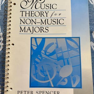 May include: A spiral-bound textbook titled Music Theory for Non-Music Majors by Peter Spencer. The cover is cream-colored with a blue vertical stripe on the right and a central blue square graphic featuring white musical notes and symbols.