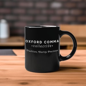 Pode incluir: Uma caneca de cerâmica preta com o texto "OXFORD COMMA • collective • Tradition, Clarity, Precision" em branco. A caneca tem uma alça curva e está sobre uma superfície de madeira.