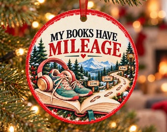 May include: A round Christmas ornament featuring the text "MY BOOKS HAVE MILEAGE" above an illustration of a pair of teal and orange sneakers resting on an open book, with red headphones, a winding path with distance markers, and mountains.