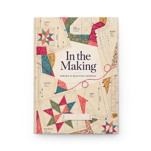 Könnte beinhalten: Ein rechteckiges Näh- und Quilt-Journal mit dem Titel In the Making. Das Cover hat einen cremefarbenen Hintergrund mit aufgedruckten Schnittmustern, gestrichelten Linien und bunten, sternförmigen Quiltblock-Illustrationen in Rot, Grün und Blau.