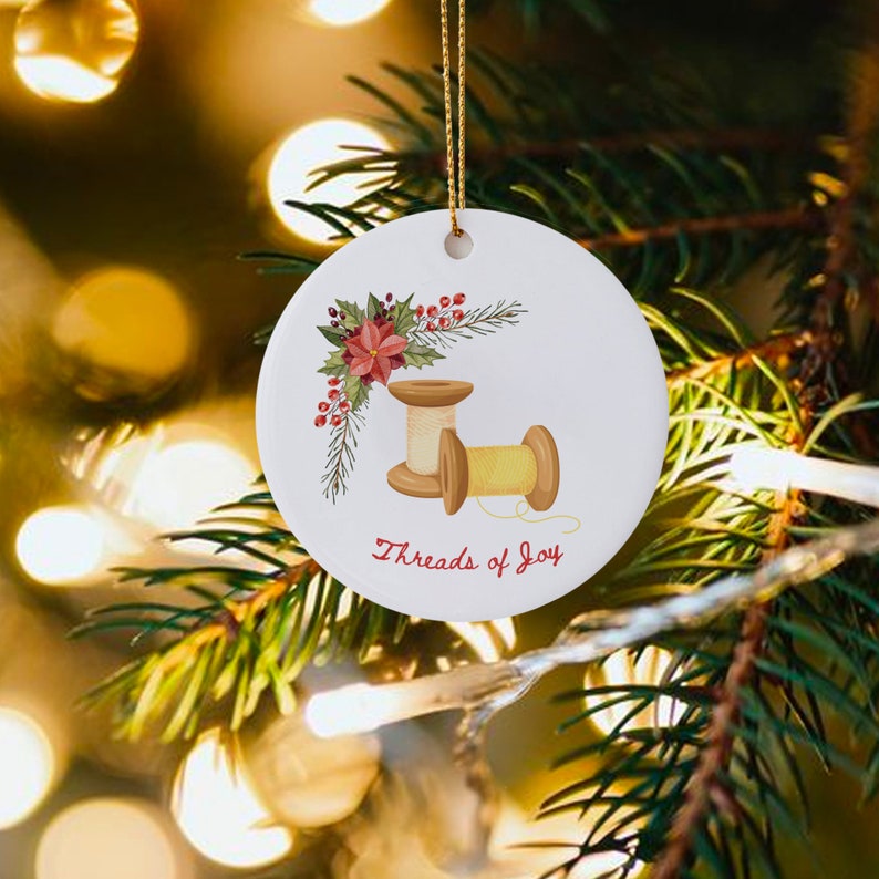 May include: A white ceramic Christmas ornament with a red poinsettia and green holly leaves. Two wooden spools of thread are shown with the text "Threads of Joy".