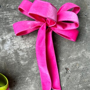 以下が含まれることがあります： ステッチされたエッジを持つ鮮やかなピンクのベルベットのリボン。リボンは長く流れるようなテールがあり、装飾やギフト包装に使用される可能性があります。明るい色と柔らかい質感が視覚的に魅力的です。