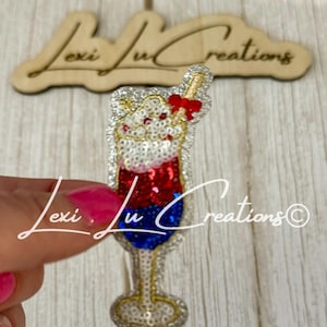 May include: A sequined cocktail glass pin with red, white, and blue layers, topped with whipped cream and a red bow. The pin is held by a hand with pink nail polish. The background includes the text "Lexi Lu Creations".