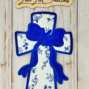 May include: A white cross with a blue floral pattern and a large blue bow. The cross is outlined in blue.
