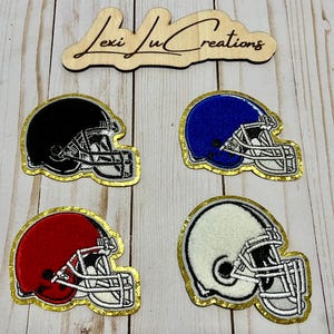 May include: Four embroidered football helmet patches in black, blue, red, and white with gold edging. The helmets have white face masks. A wooden sign at the top reads "Lexi Ju Creations".