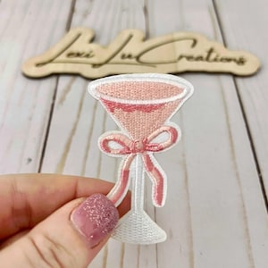 May include: Pink embroidered iron-on patch of a martini glass with a pink bow.