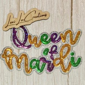 May include: A wooden sign with the text "Lexi Lu Creations" above a sequined "Queen of Mardi" design. The design features gold, green, purple, and silver glitter accents, perfect for Mardi Gras celebrations.