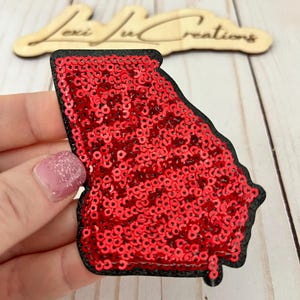 May include: Red sequin iron-on patch in the shape of the state of Georgia. The patch has a black outline.