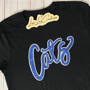May include: Black t-shirt with a blue and white "Cats" design made of rhinestones.