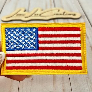 May include: Embroidered American flag patch with a yellow border. The flag features a blue field with white stars and red and white stripes. The patch is rectangular and appears to be new.
