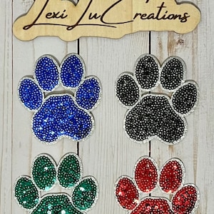 May include: Four sequined paw print iron-on patches in blue, black, green, and red.  The patches are approximately 3 inches in diameter.