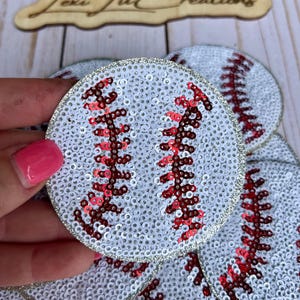 May include: Baseball-themed sequin patches. Each patch is round, white, and covered in sequins. Red sequin stitching mimics the baseball's seams. A silver glitter border surrounds each patch. The patches are ideal for crafting and embellishments.