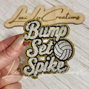 May include: A decorative patch featuring the text Bump Set Spike in white sequins with black outlines and gold sequin borders. A white and black sequin volleyball icon is positioned to the right of the word Set. The patch has a layered design.