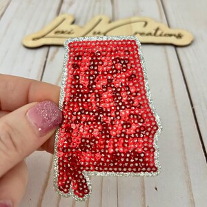 May include: Red sequin iron-on patch in the shape of the state of Alabama with a silver glitter outline.