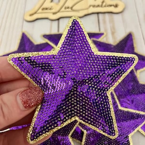 May include: Purple star-shaped sequins with a gold glitter trim. The sequins are sewn together to create a patch.