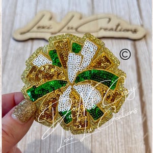 May include: A gold, green, and white sequined flower-shaped embellishment. The design features a circular pattern with gold sequins outlining the edges, green and white sequins filling the interior, and a glittery gold border. The text "Lexi Lu Creations" is visible.