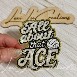 May include: A decorative patch featuring the text All about that ACE in white sequins with a black outline and gold sequin border. A white and black volleyball graphic is positioned to the right of the word that. The patch has a layered design.
