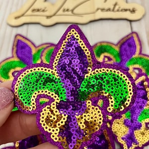 May include: Purple, green, and gold sequined fleur-de-lis patches. The patches are made of sequins and have a shiny finish.