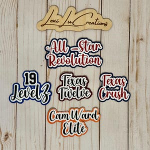 Peut inclure: Découpes en bois avec du texte, dont "All-Star Revolution", "Texas Crush" et "Cam Ward Elite". Les découpes sont de différentes couleurs, comme le rouge, le bleu et l'orange, avec des accents de paillettes. Un panneau en bois avec le texte "Lexi Lu Creations" est en haut.