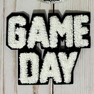 May include: White felt letters spelling "GAME DAY" with black outlines. The letters are raised and have a fuzzy texture.