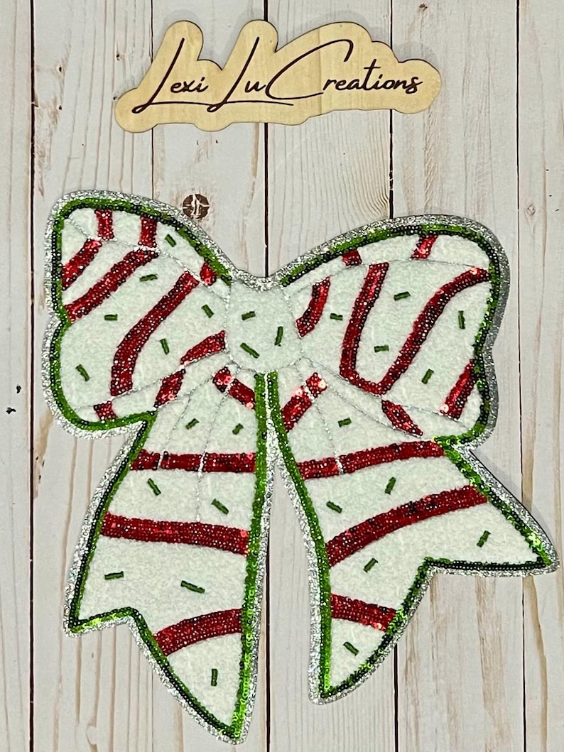 Pu&ograve; includere: Un fiocco natalizio decorativo con base bianca, strisce rosse e bordi di paillettes verdi e argentate. Il fiocco ha un aspetto strutturato ed &egrave; impreziosito da piccole perline verdi. Il cartello in legno sopra il fiocco recita "Lexi Lu Creations."