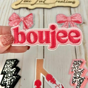 May include: Pink and white embroidered patch with the word "boujee" in red lettering.