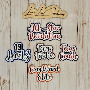 May include: Wooden cutouts with text, including "All-Star Revolution," "Texas Crush," and "Cam Ward Elite." The cutouts are in various colors, such as red, blue, and orange, with glitter accents. A wooden sign with the text "Lexi Lu Creations" is at the top.