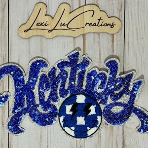 May include: Blue and silver sequined iron-on patch with the word "Remarkable" and a blue and white checkered smiley face with lightning bolts.