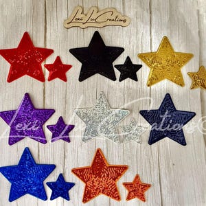 May include: A collection of star-shaped patches in various colors including red, black, gold, purple, silver, navy blue, royal blue, and orange. Each color features a large and small star, all with a textured, sequined finish. The text Lexi Lu Creations is visible.