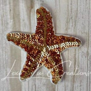 May include: A sequined starfish applique in shades of gold and copper, with a white border. The starfish is covered in small, shiny sequins, creating a textured and eye-catching design. Perfect for embellishing clothing or accessories.