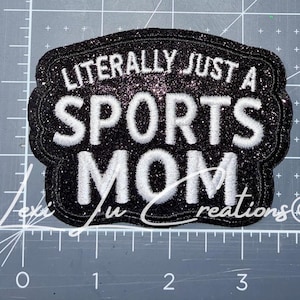 May include: Black glitter patch with white embroidered text that reads "LITERALLY JUST A SPORTS MOM". The patch has a decorative border and is likely for apparel or accessories.