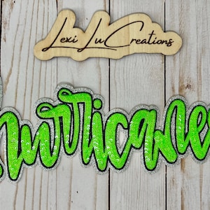 May include: A sequined patch with the word "Hurricanes" in bright green script, outlined in black and silver glitter. A wooden sign above reads "Lexi Lu Creations" in cursive.