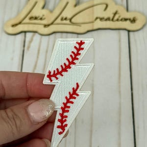May include: White lightning bolt patch with red baseball stitching. The patch is held in a hand. A wooden sign with the text "Lexi Lu Creations" is in the background.
