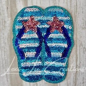 May include: A pair of sequined flip-flops in shades of blue and white, adorned with two sparkling pink starfish. The flip-flops have dark blue straps and are designed with a glittery finish, perfect for a beach or summer theme.