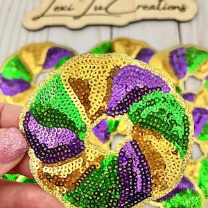 May include: A Mardi Gras themed donut shaped sequin patch with gold, green, and purple sequins.