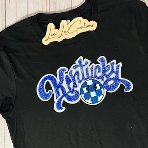 May include: Black t-shirt with a blue and white sparkly "Kentucky" graphic with a smiley face.