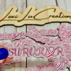 Op de afbeelding: Roze geborduurde "SURVIVOR" patches met een roze lint ontwerp op een witte achtergrond. De afbeelding toont ook een houten bord met de tekst "Lexi Lu Creations". Geschikt voor kleding of accessoires.