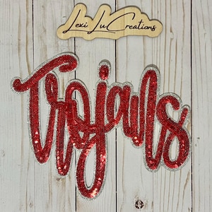 May include: Red and silver sequined iron-on patch with the word "Trojans" in a cursive font.