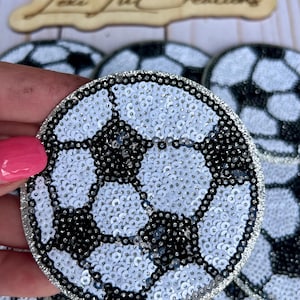 May include: A close-up of a black and white soccer ball patch made of sequins. The patch is round and has a silver border.