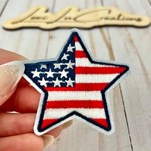 May include: Embroidered star patch featuring the American flag design. The patch has a blue border and a white, red, and blue color scheme. The patch is in the shape of a star and is likely for clothing or accessories.