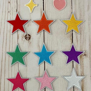 May include: A collection of colorful star-shaped patches in various colors, including red, orange, green, blue, purple, pink, and silver, with white borders. Also included are a yellow starburst and a pink heart. The wooden sign above reads "Lexi Ju Creations."