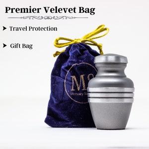May include: A silver metal cremation urn with a velvet bag. The urn has three bands around it. The bag is blue with a gold drawstring and the text "Mortuary Services" on it.