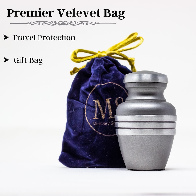 May include: A silver metal cremation urn with a velvet bag. The urn has three bands around it. The bag is blue with a gold drawstring and the text "Mortuary Services" on it.