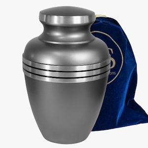 May include: A gray metal cremation urn with a silver trim and three bands around the middle. The urn comes with a blue velvet carrying bag.