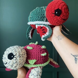 Può includere: Due peluche di tartaruga all'uncinetto. Uno è rosso con un guscio verde e l'altro è rosa con un guscio bianco e nero.