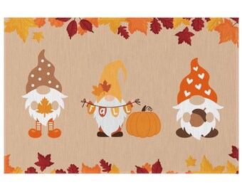 Puede incluir: Tres gnomos con decoraciones de otoño. El gnomo de la izquierda lleva un sombrero marrón con lunares blancos y sostiene una hoja. El gnomo del medio lleva un sombrero amarillo y sostiene una pancarta que dice "otoño". El gnomo de la derecha lleva un sombrero rojo con corazones blancos y sostiene una pequeña calabaza. Hay una calabaza delante de los gnomos.