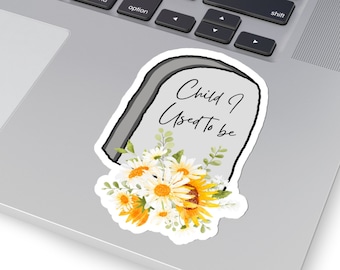 Puede incluir: Una lápida blanca con el texto "Child I Used To Be" en escritura negra. La lápida está decorada con un ramo de margaritas blancas y girasoles amarillos.