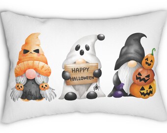 Puede incluir: Una almohada blanca con un tema de Halloween con tres gnomos. Un gnomo es un fantasma que sostiene un cartel que dice "Feliz Halloween". Otro gnomo lleva un sombrero negro y sostiene una pila de calabazas. El tercer gnomo lleva un sombrero naranja y sostiene una calabaza en cada mano.
