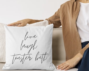 Puede incluir: Cojín blanco con texto en cursiva negra que dice "live laugh toaster bath".
